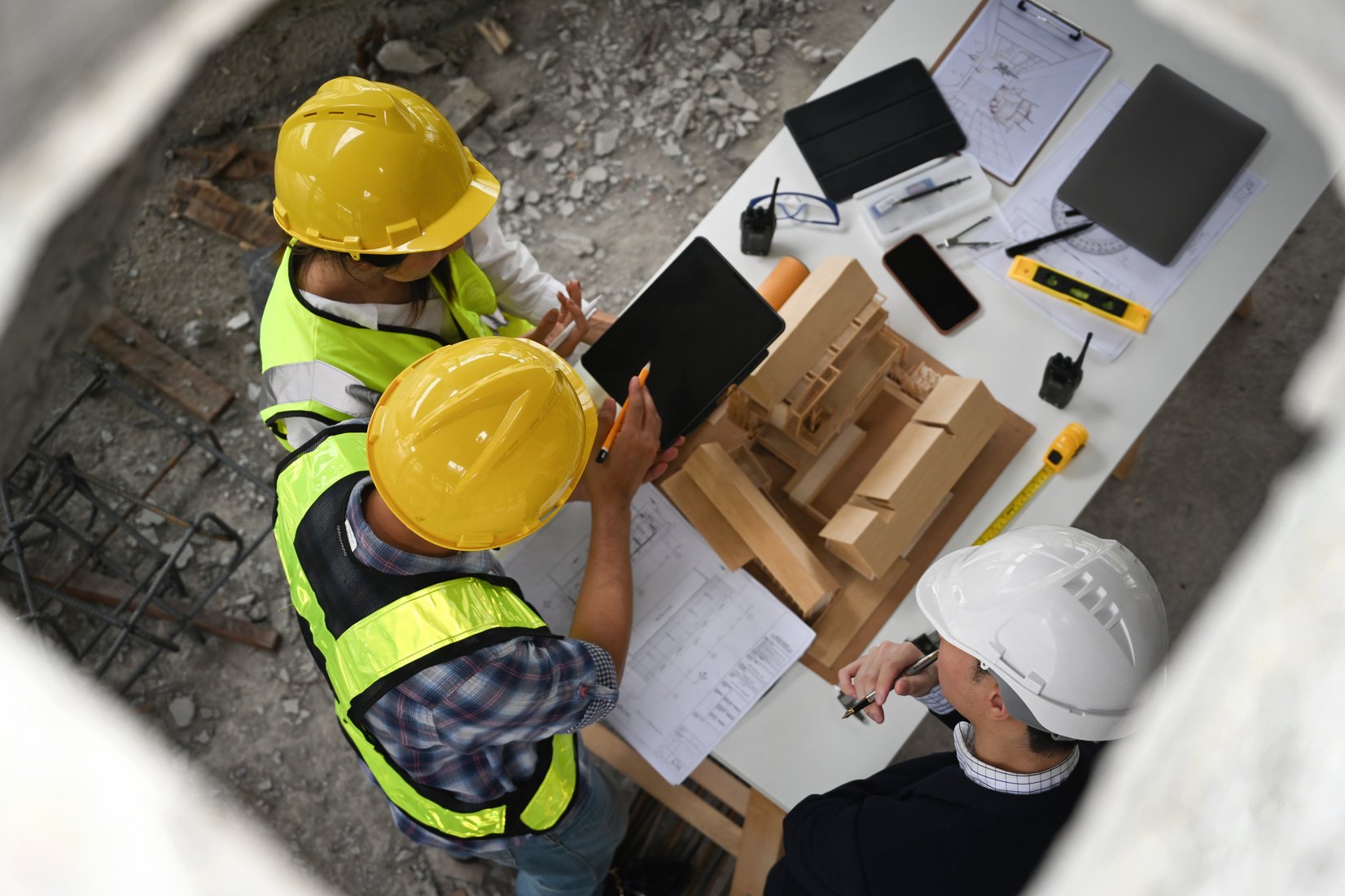 Top view of a manager and workers reviewing construction plans and a building model at a site table, Comprehensive oversight and teamwork in construction project planning and execution